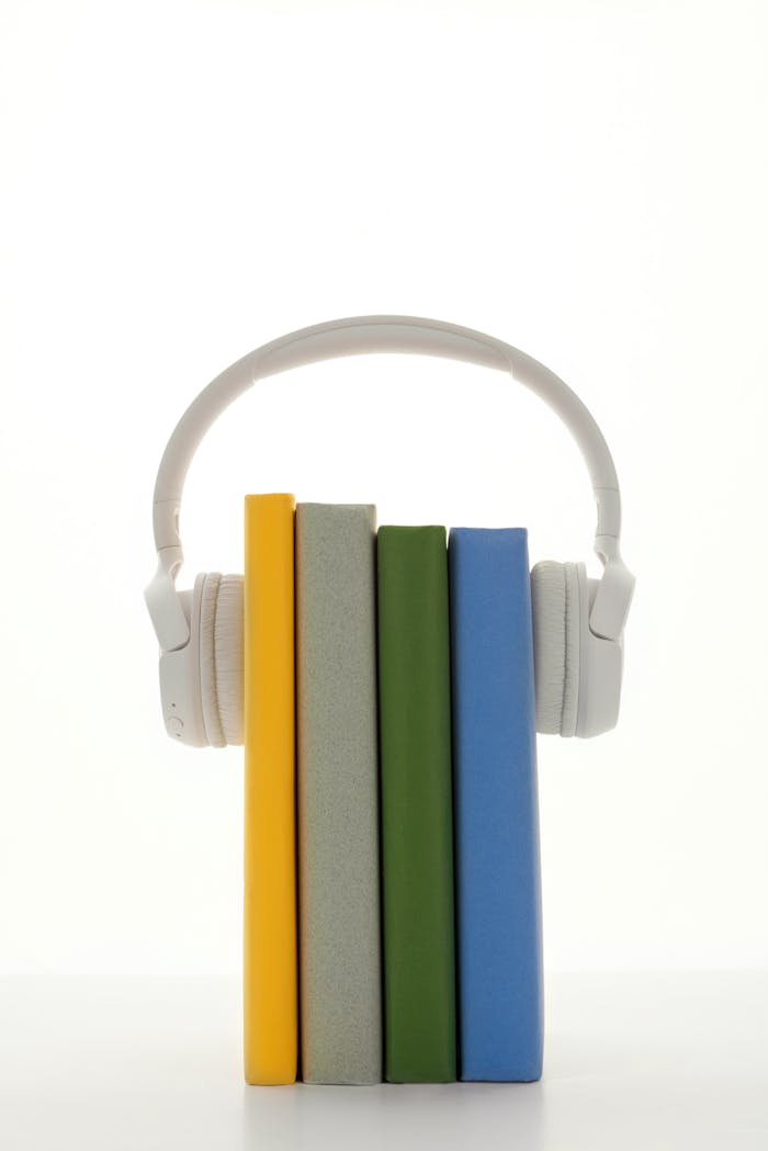 A stack of colorful books with headphones, symbolizing audio learning on a white background.